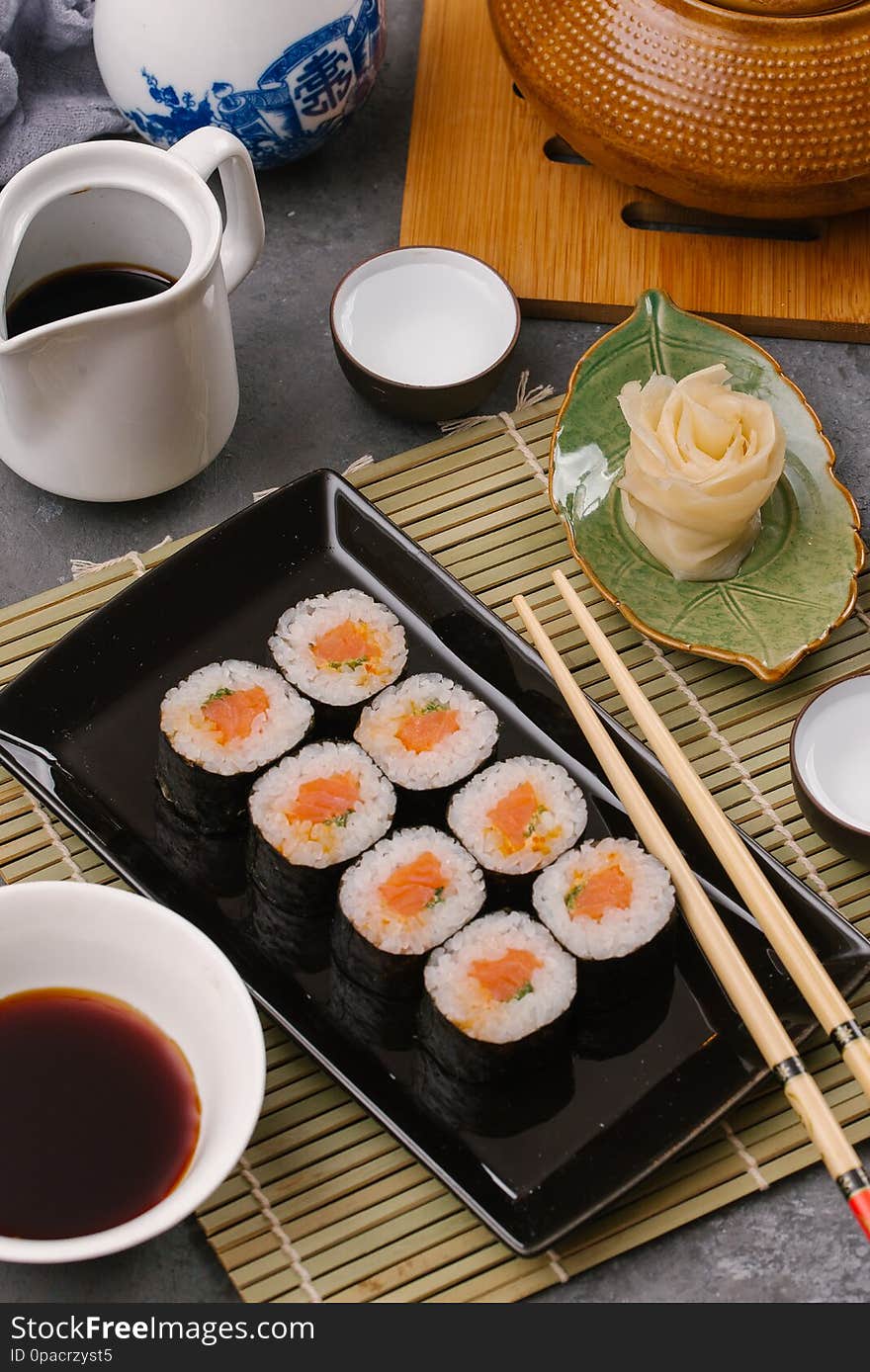 Japanese restaurant, sushi roll on black slate plate. Set for one person with chopsticks, ginger, soy, top view, copy