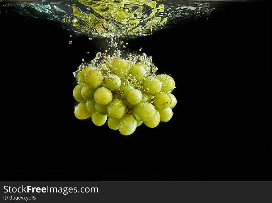 Fresh green grapes bunch splashing into water. Isolated on black background. Fresh green grapes bunch splashing into water. Isolated on black background