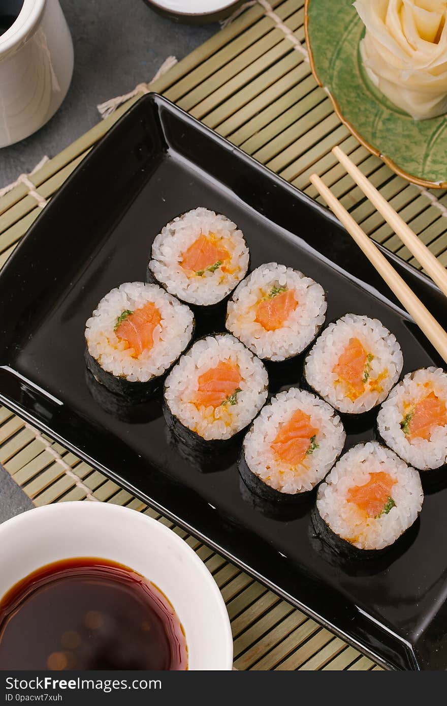 Japanese restaurant, sushi roll on black slate plate. Set for one person with chopsticks, ginger, soy, top view, copy