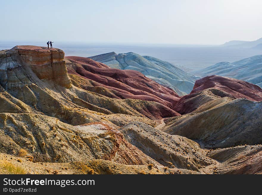 Travelers stand on the edge of a cliff against the backdrop of an epic desert mountain landscape