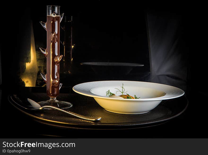 Vegetarian soup with mushrooms, mozzarella cheese, and dill served in restaurant white plate and spoon on black background