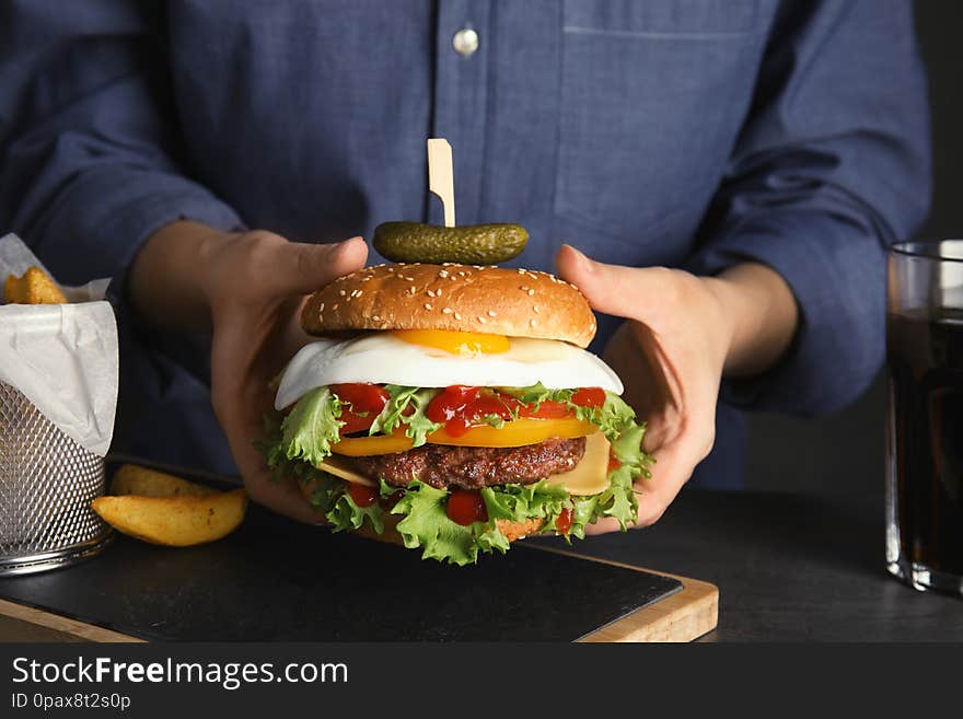 Woman holding tasty burger with fried egg over table