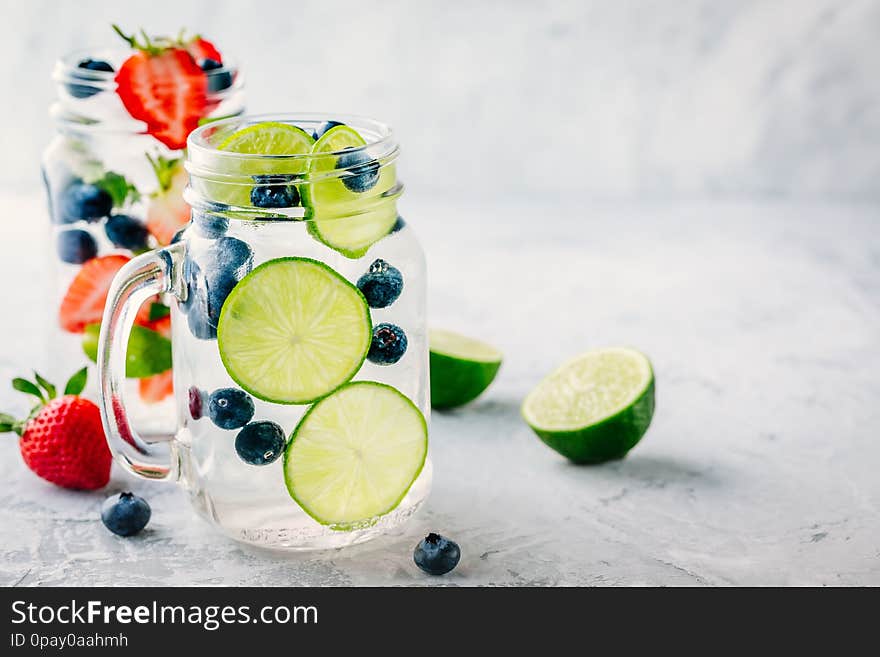 Infused detox water with green lime slices and blueberry. Iced cold summer cocktail or lemonade in glass mason jar