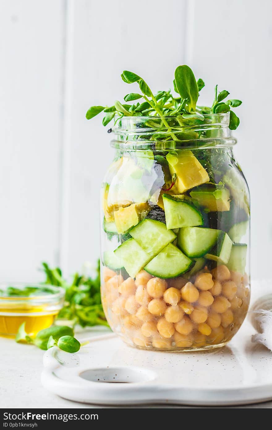 Green salad with chickpeas in a jar, white background, copy space