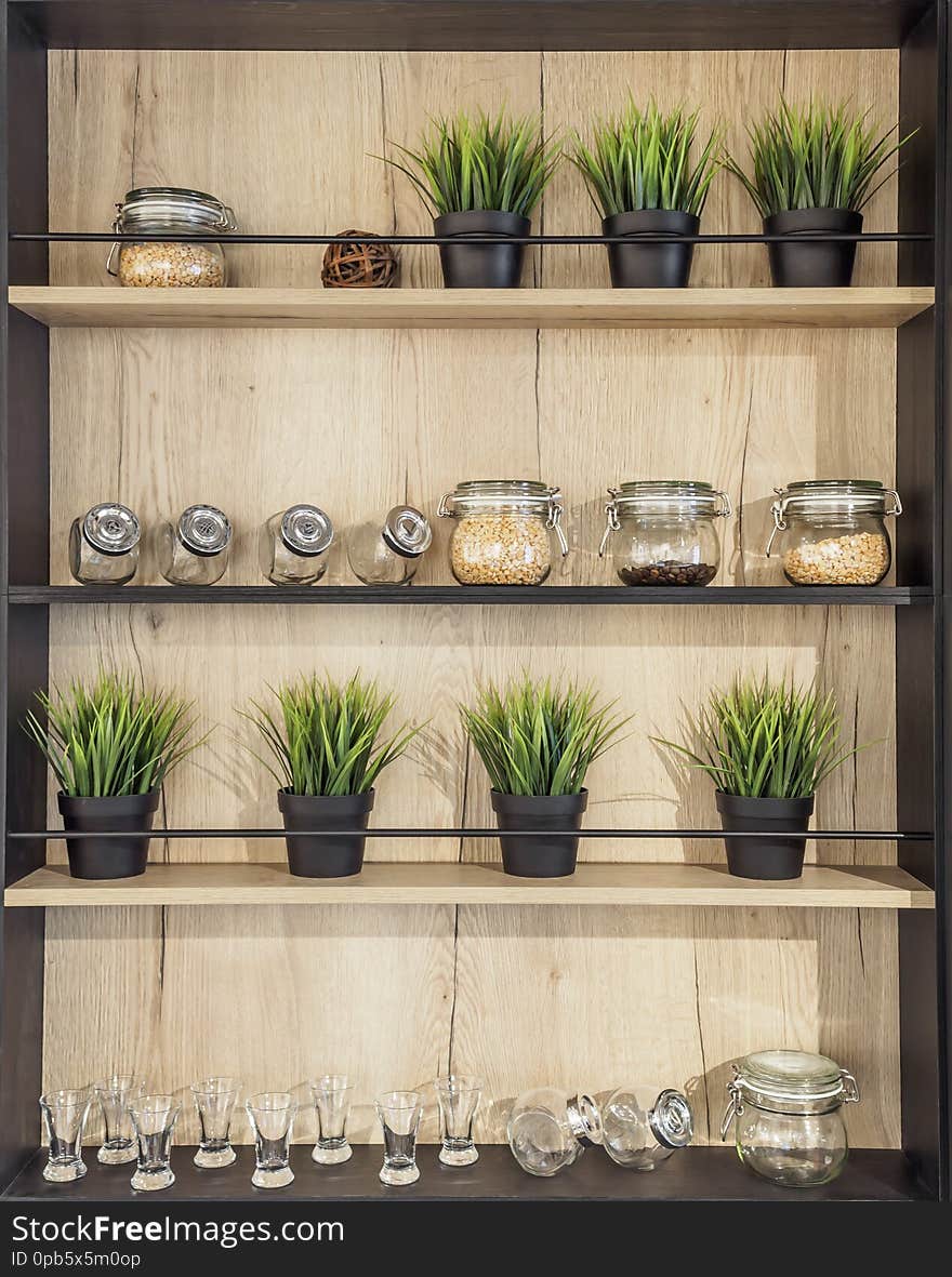 Wooden helf with kitchenware. Glass jars with spices pot plant glasses on the wooden rack kitchen background