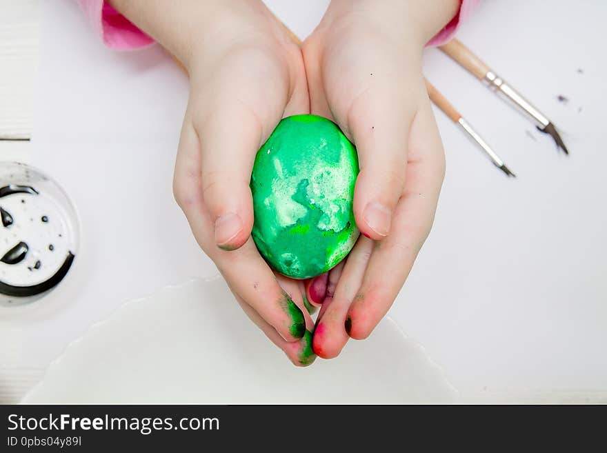 A flat lay with kid`s hands painting Easter eggs on a white wooden table