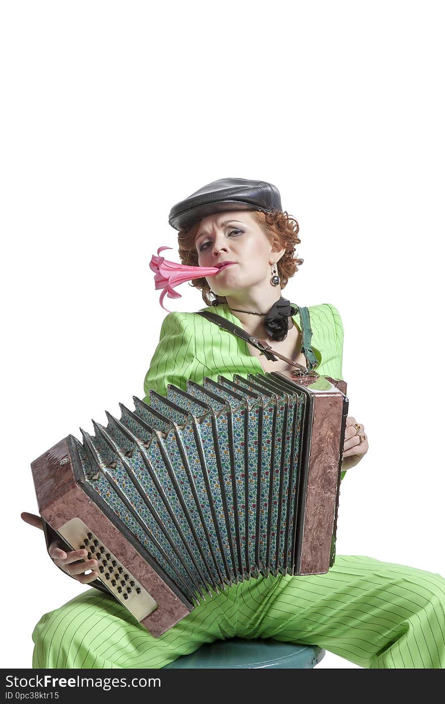 A young woman in a green pantsuit with a cap on her head and a flower in her teeth playing Russian fur accordion. A young woman in a green pantsuit with a cap on her head and a flower in her teeth playing Russian fur accordion