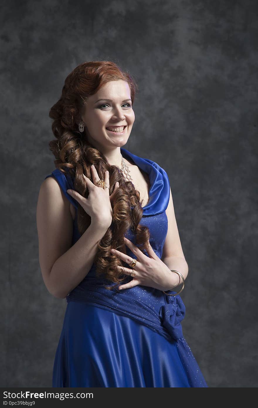 Young woman in a dark blue classic evening dress posing in the studio on a gray background. Young woman in a dark blue classic evening dress posing in the studio on a gray background