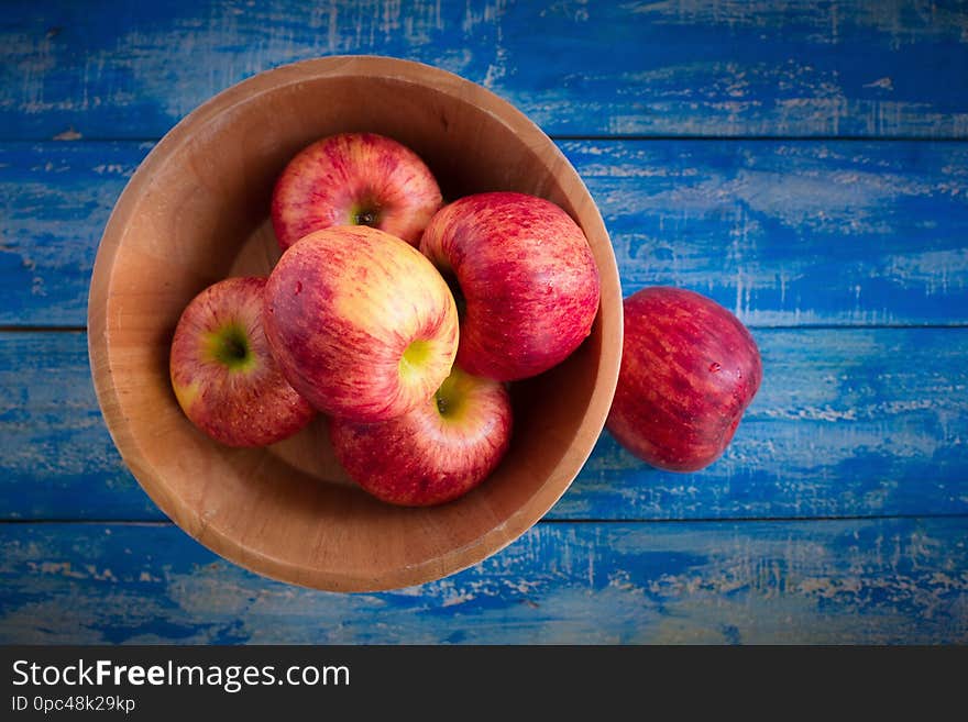 Red apples in a wooden bowl on a blue wooden background