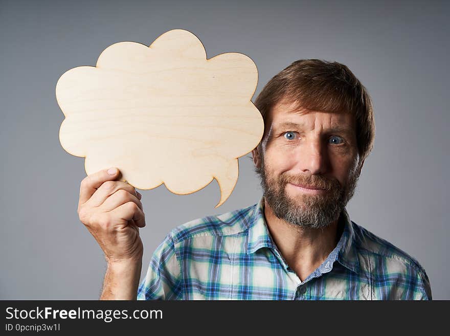 Mature man in checkered shirt holding speech bubble looking at camera, over grey studio background. Mature man in checkered shirt holding speech bubble looking at camera, over grey studio background