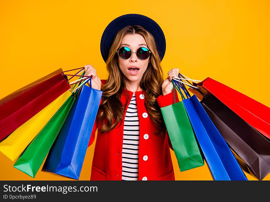 Portrait of shocked charming elegant adorable curly-haired lady in eyeglasses eyewear holding many colorful bags wearing fall modern outfit isolated over yellow background