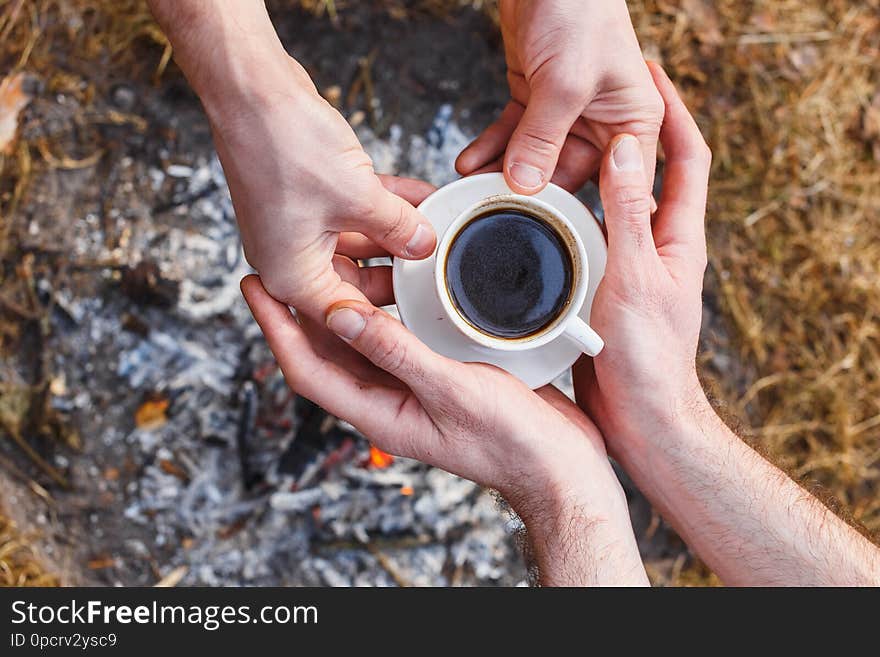 Lovers of men make coffee on the fire in the Turk. In the frame, the hands of one person pass a cup to a friend