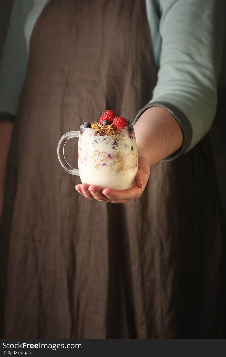 Woman holding a glass jar with Granola, Yogurt And berries. Vertical.