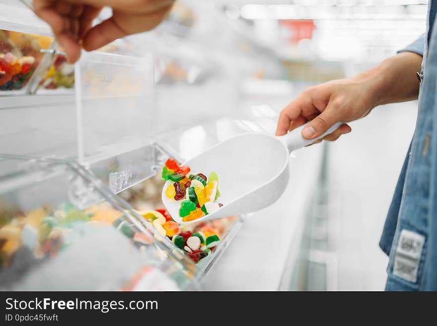 Male person picks up a package of chewy candy in a supermarket, family shopping. Customer buys marmalade in shop, buyer in market, sweets department. Male person picks up a package of chewy candy in a supermarket, family shopping. Customer buys marmalade in shop, buyer in market, sweets department