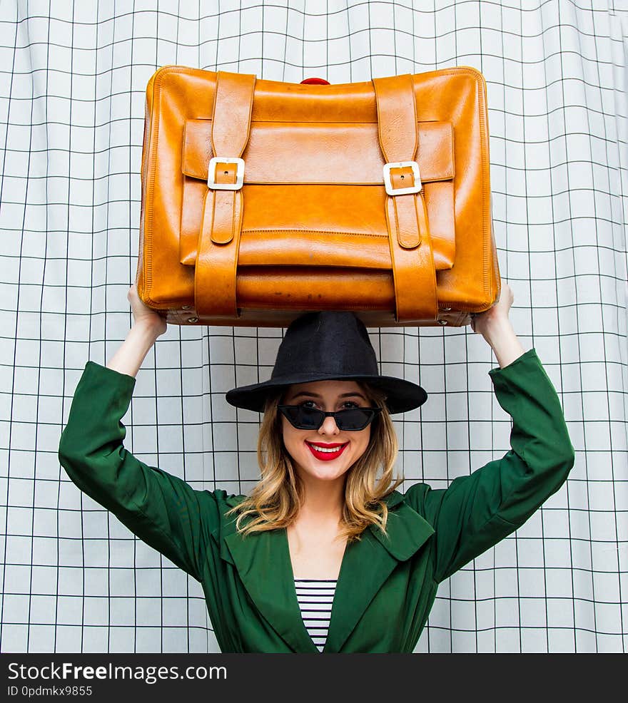 Young style woman in hat and green cloak in 90s style with travel suitcase stay on checkered background