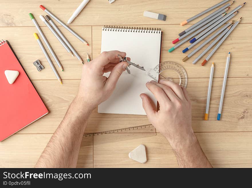 The designer draws a sketch in a notebook on a wooden table. Stationery. View from above