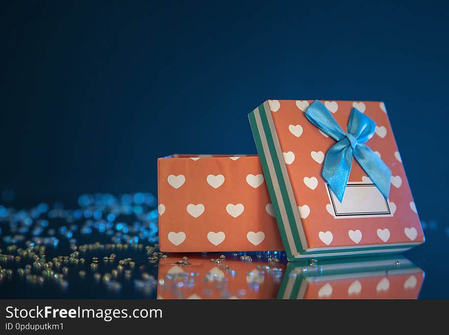 Photography of beautiful pink-white gift box who is standing on a mirror, among rhinestones