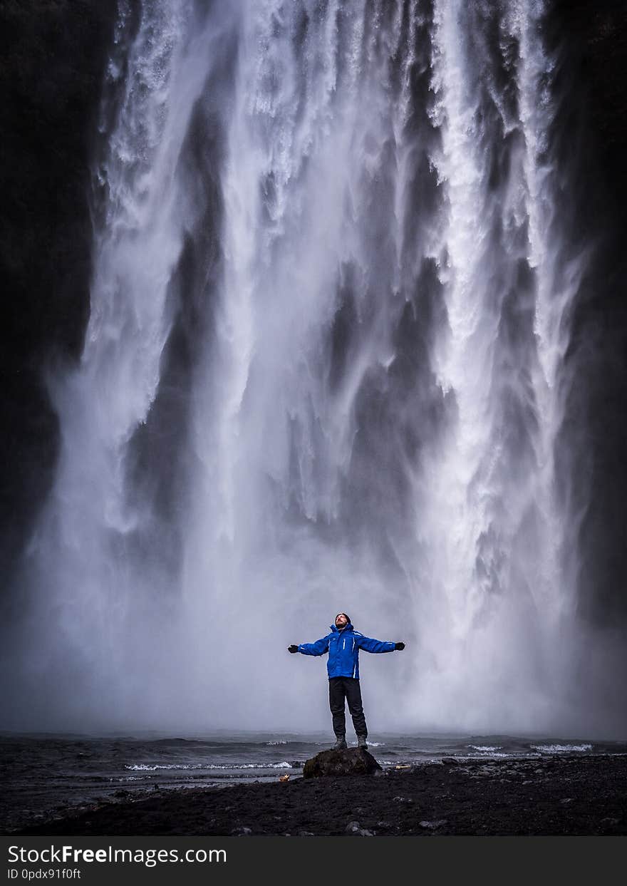 Male tourist in warm clothes stretching out arms and standing near Skogafoss Waterfall in Iceland. Male tourist in warm clothes stretching out arms and standing near Skogafoss Waterfall in Iceland