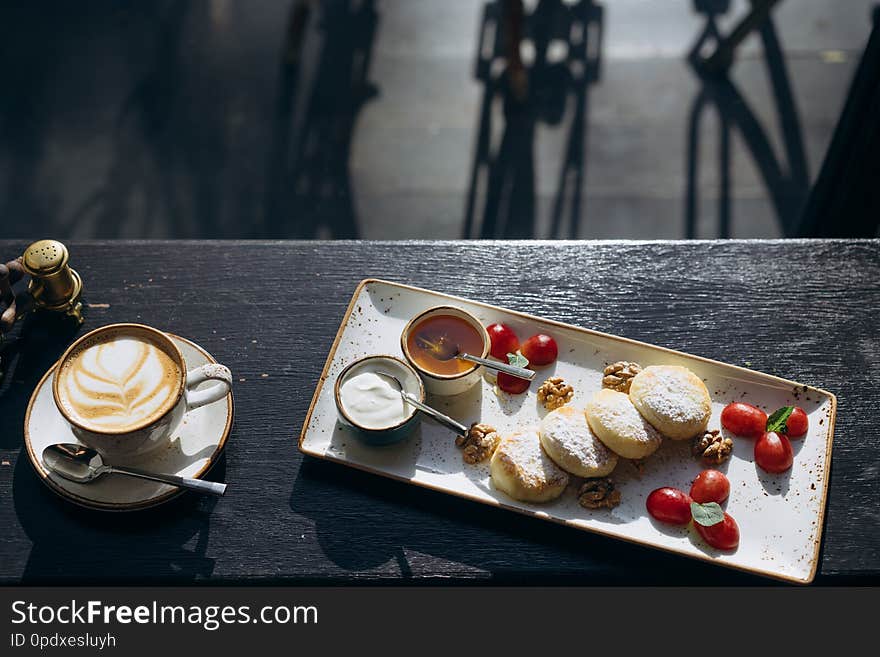 Cottage cheese pancakes with sour cream, honey on a tray and latte on the table