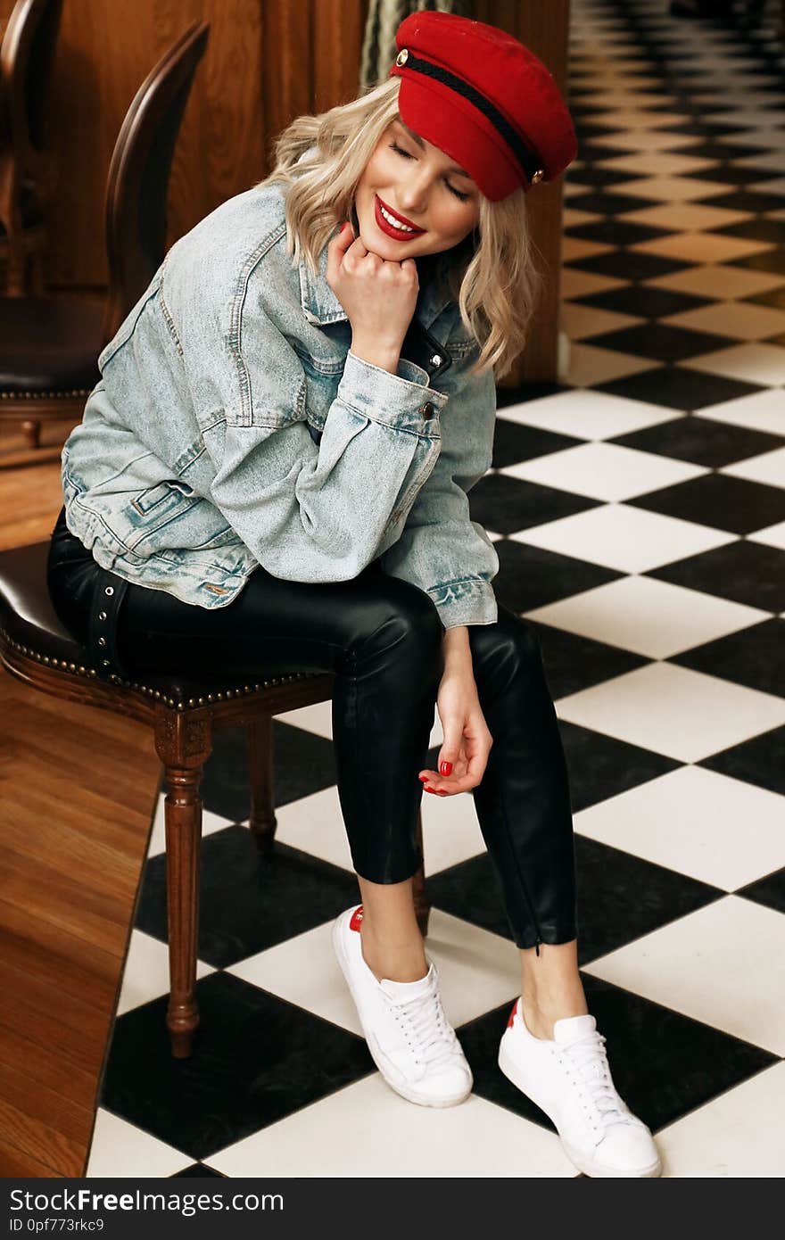 Fashion photo of beautiful woman with blond hair in casual clothes and red hat sitting in cafe