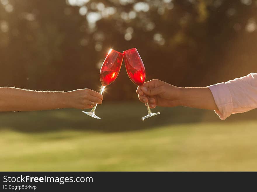 Two red wine glasses in woman hand and man hand on nature background. Summer time. Lifestyle