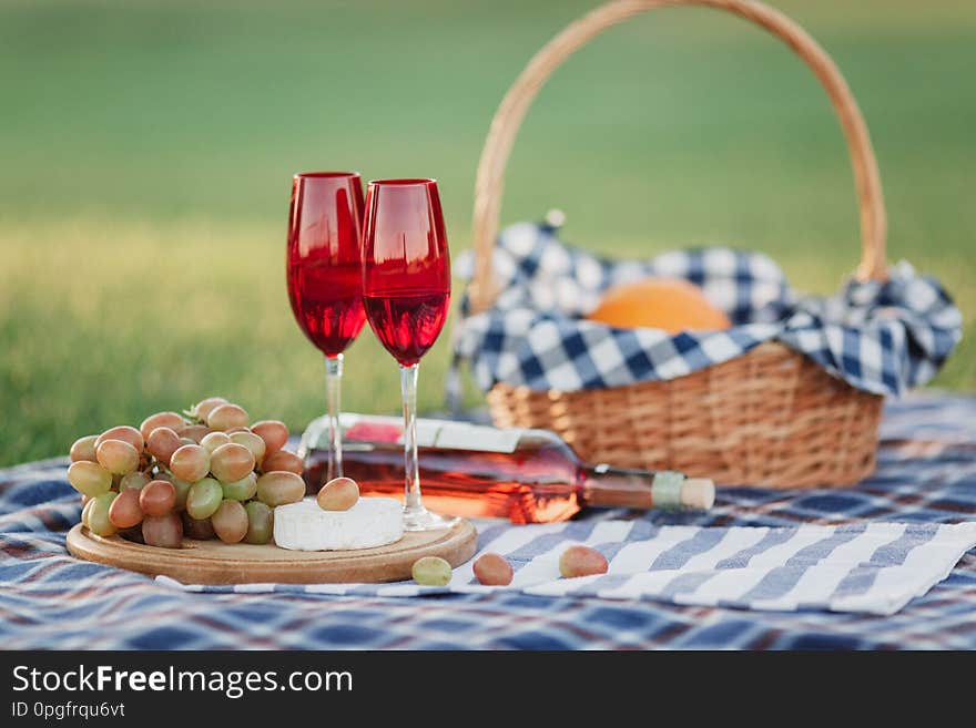 Picnic basket with drinks, food and fruit on green grass outside in summer park