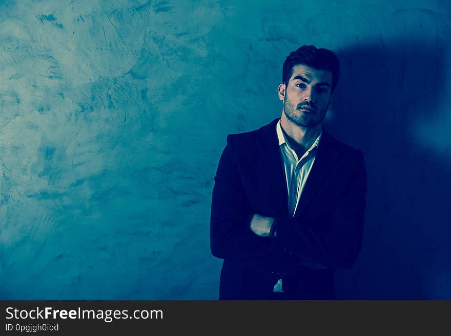 A serious handsome young businessman in a black suit standing in front of a grey wall in a studio. A serious handsome young businessman in a black suit standing in front of a grey wall in a studio.