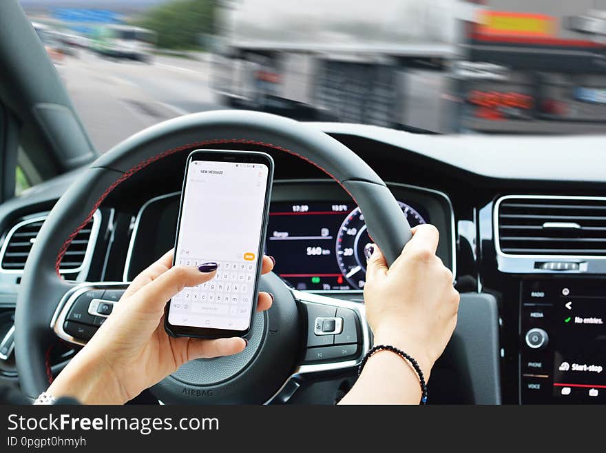 Risk of accident concept with woman texting on smartphone while driving. Risk of accident concept with woman texting on smartphone while driving