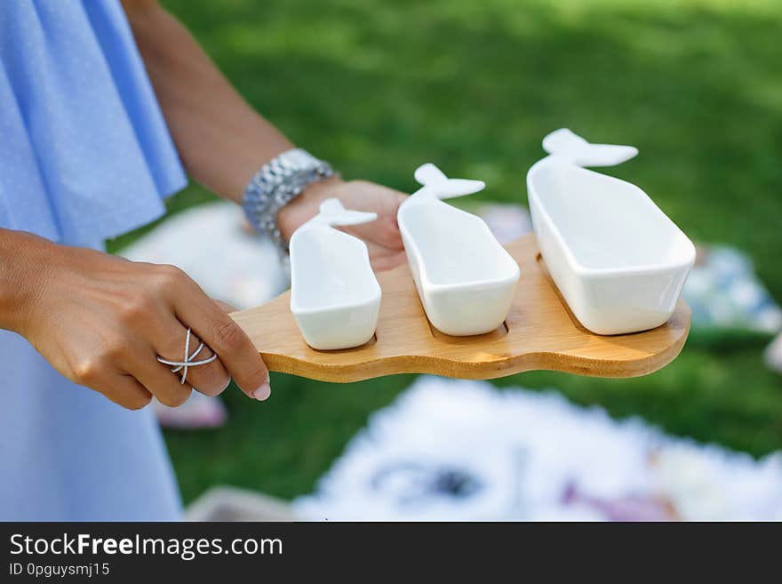 Girl with a set of white empty sauceboats on a wooden tray serves a picnic