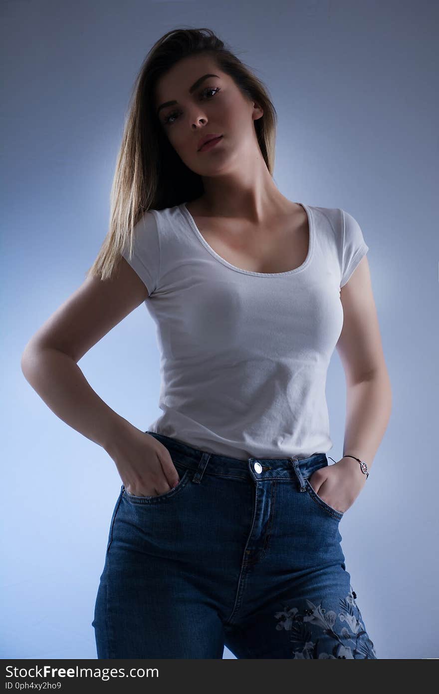 Low key girl portrait with blonde hair in white t shirt and blue jeans, looking on camera and hands in pockets. Female portrait in studio Close up. Low key girl portrait with blonde hair in white t shirt and blue jeans, looking on camera and hands in pockets. Female portrait in studio Close up