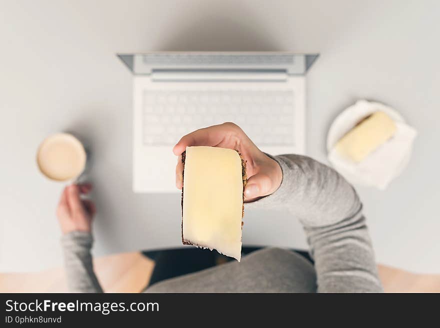 Woman having lunch break at workplace with coffee and cheese sandwich.