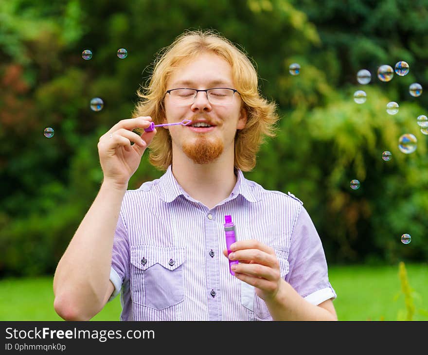 Happiness and carefree concept. Young man having fun blowing soap bubbles outdoor in park. Happiness and carefree concept. Young man having fun blowing soap bubbles outdoor in park