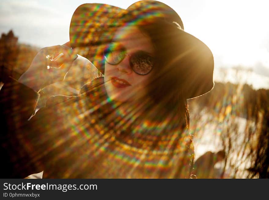 Young woman with red lips and nails posing in black coat and black hat. Woman with wild hair in windy weather. Photo with soft focus and rainbow glare on the lens. Young woman with red lips and nails posing in black coat and black hat. Woman with wild hair in windy weather. Photo with soft focus and rainbow glare on the lens