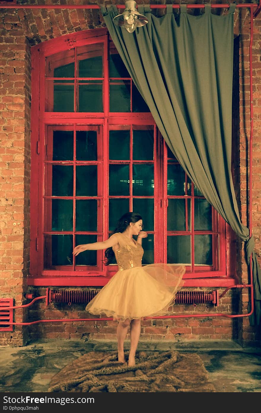 Cute girl with a smile lying in a gold dress on a fur rug near a large red window in the evening alone