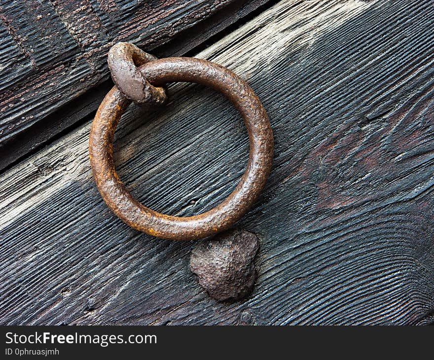 Door knocker with rust of ancient door in eroded wood. Rural house in Italy, province of Modena.