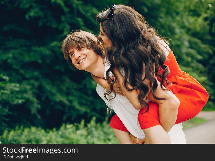 Pretty brunette with her boyfriend. Couple in a summer park. Lady in a red dress. Pretty brunette with her boyfriend. Couple in a summer park. Lady in a red dress