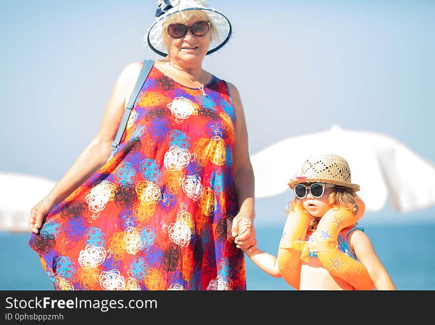 Adorable little girl wearing sunglasses, inflatable over-sleeves floats and inflatable donut float ring standing at the beach with