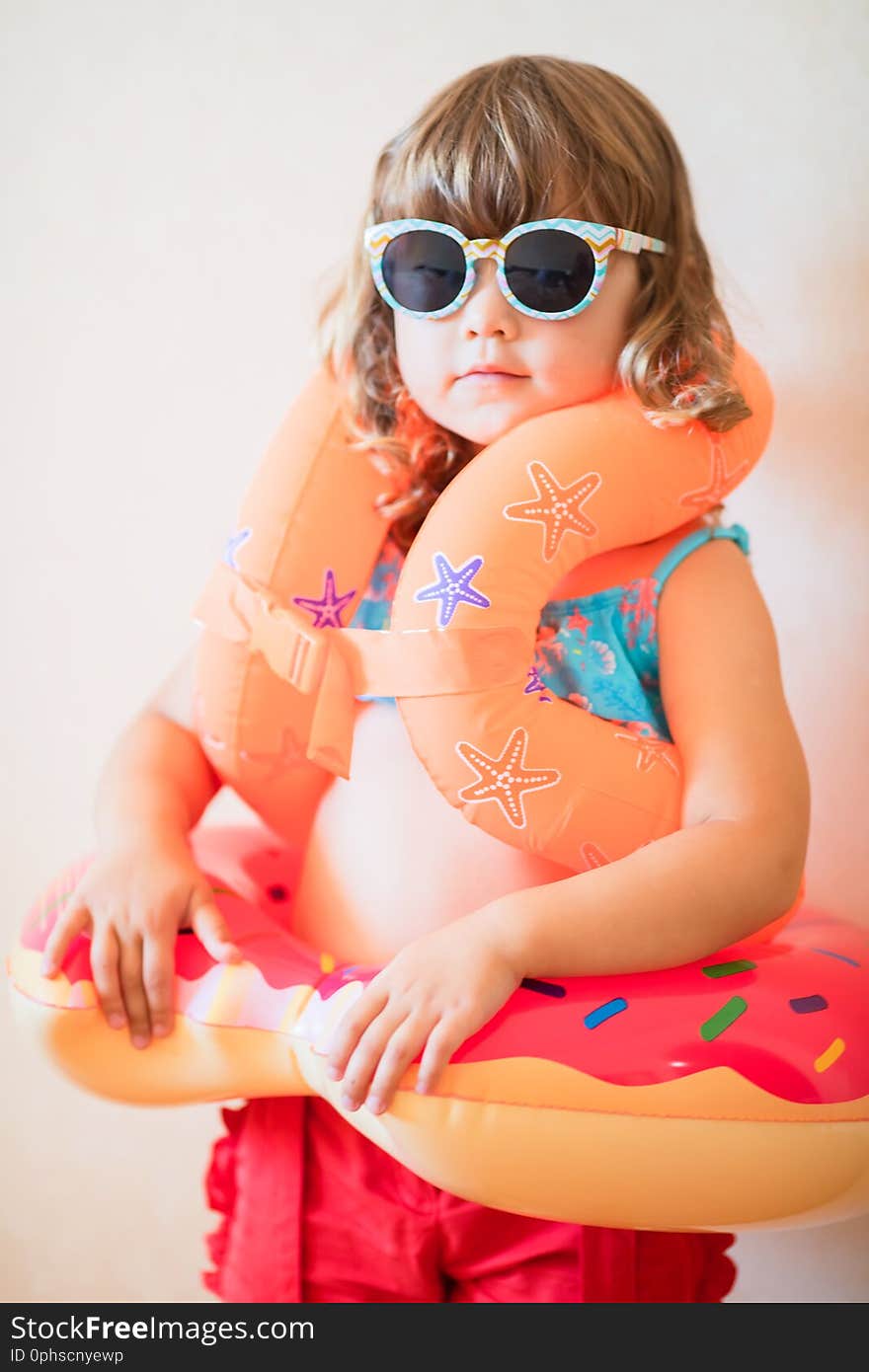 Adorable little girl ready to go for the beach, wearing sunglasses, inflatable over-sleeves floats and inflatable donut float ring