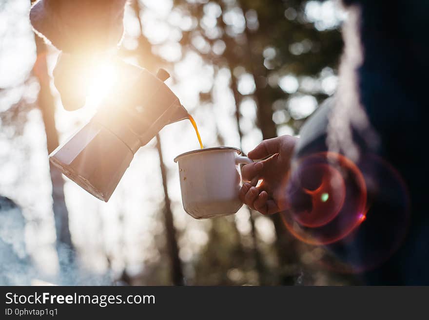 Outdoor shot of young woman pours itself hot beverage in mountains near to bonfire during the sunset.