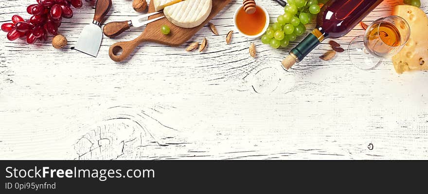 White wine bottle, grape, honey, cheese and wineglass on white wooden board. Panoramic top view with copy space for your text