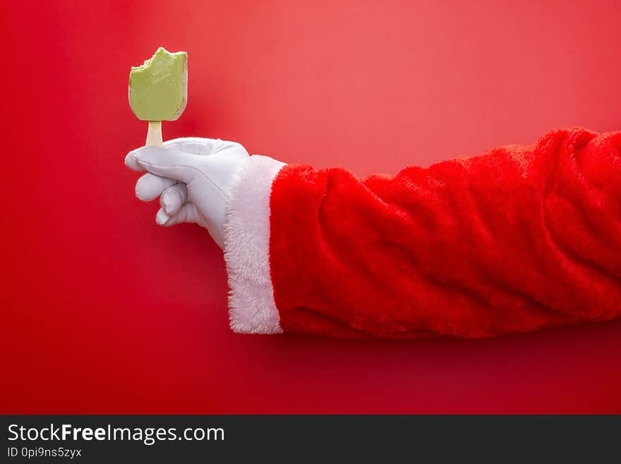 Santa claus holding green bean popsicle with some bites in front of a red background