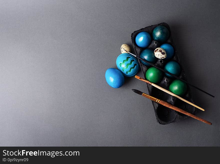 Easter holiday: colored painted eggs in a black box and a brush against a dark background.