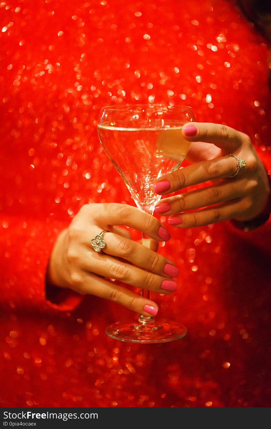 Glass hand girl. White wine in the glass and girl in a sparkling red dress close-up. Celebration and party in a nightclub. Chic red dress. Drinks for adults. Beautiful bokeh and soft focus.