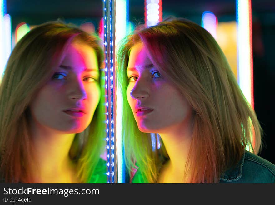 Sweet caucasian girl walks in a mirror maze with colorful diodes and enjoys an unusual attraction room in the city