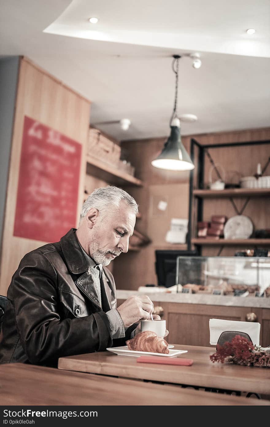 Serious gray-haired man sitting alone in cafeteria