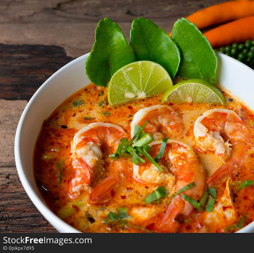 Shrimp soup or Tom Yam goong  in a white dish local food in Thailand consisting of chili lemon ginger galangal lemon grass lemon leaf on the old wood background. Shrimp soup or Tom Yam goong  in a white dish local food in Thailand consisting of chili lemon ginger galangal lemon grass lemon leaf on the old wood background.