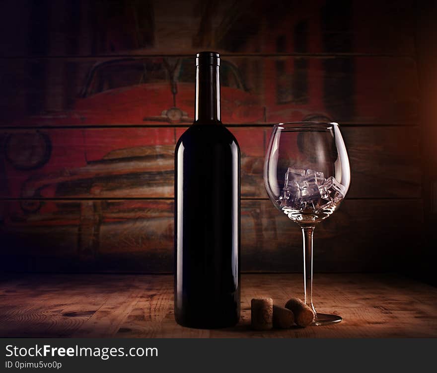 A bottle of wine and an empty wine glass with ice. on a wooden table.