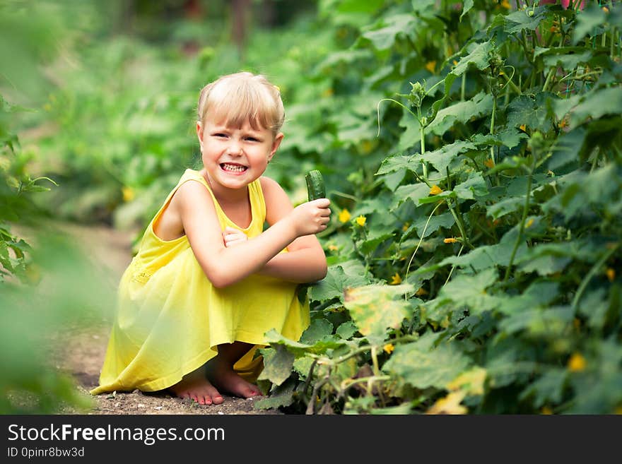 Little girl in a yellow dress curled up eating bitter cucumber. Little girl in a yellow dress curled up eating bitter cucumber