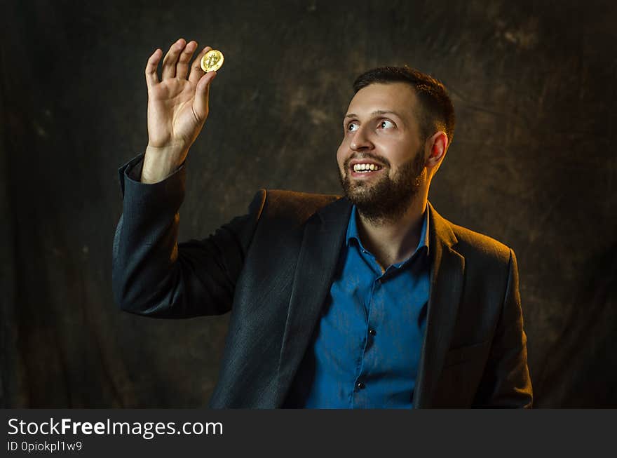 A young businessman holds a coin of bitcoite in his hand