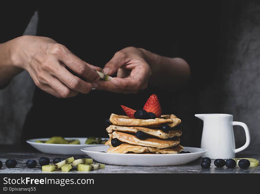 Woman housewife preparing pancakes to be food for family, putting topping fruit, strawberries, kiwi and blueberries on top. Woman housewife preparing pancakes to be food for family, putting topping fruit, strawberries, kiwi and blueberries on top